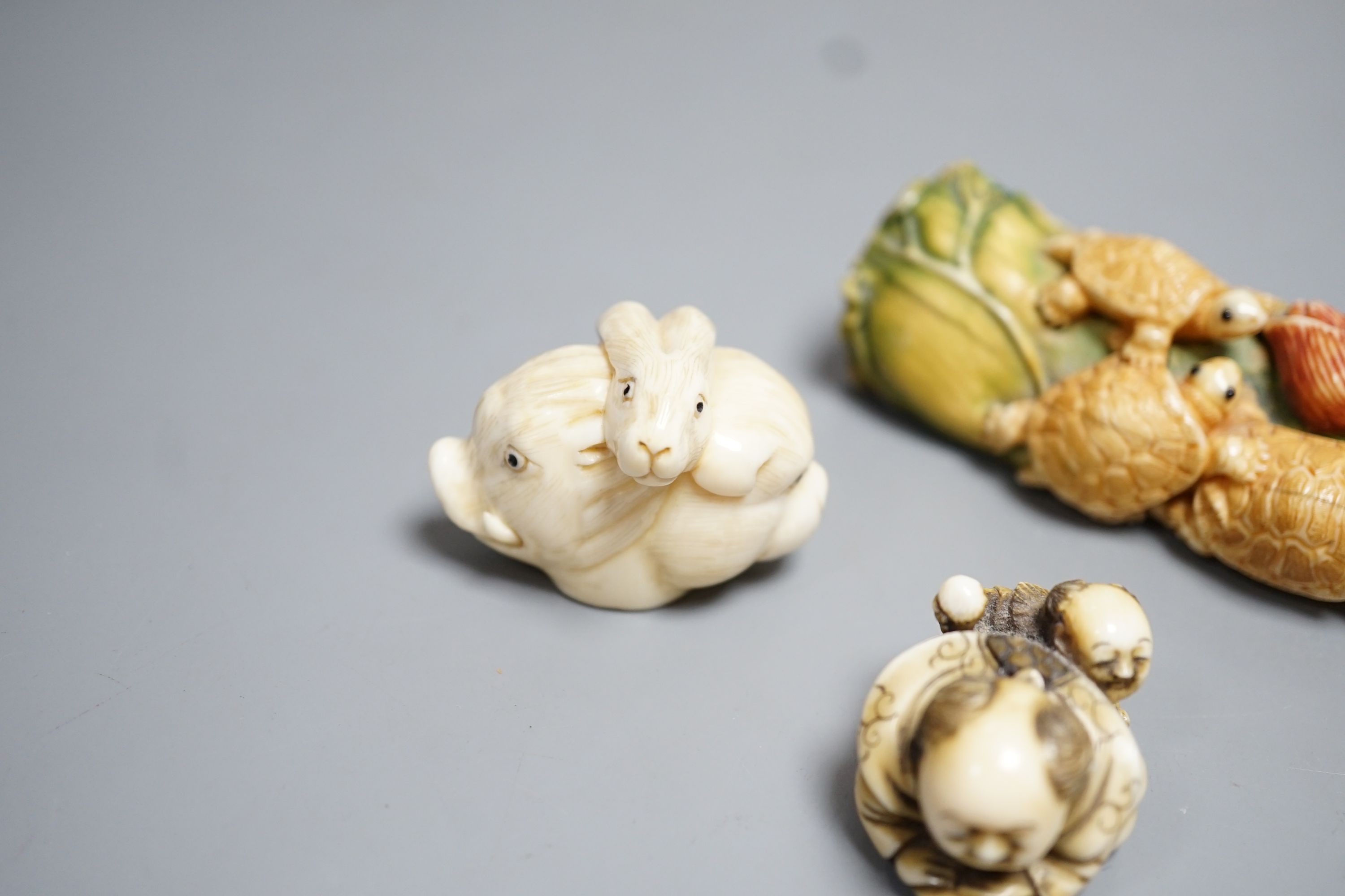 A Japanese ivory Netsuke of two boys holding a noh mask, an ivory Netsuke in the form of three animal heads and a coloured Ivory carving of tortoises on a lotus leaf, all singed (3) largest 12cm